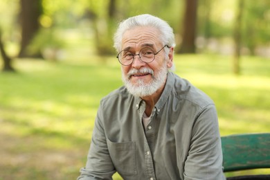 Portrait of happy grandpa with glasses on bench in park