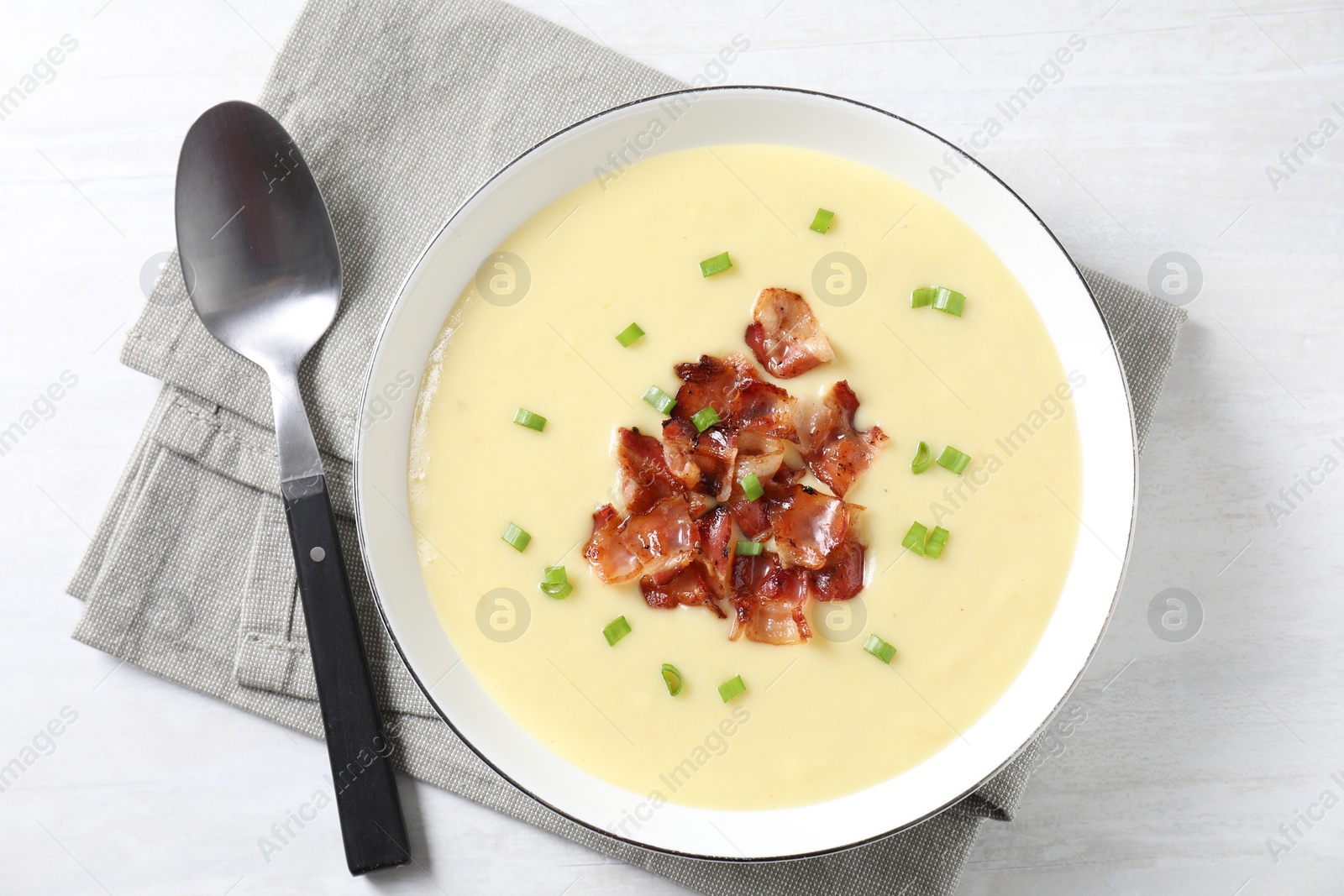 Photo of Tasty potato soup with bacon in bowl and spoon on white wooden table, top view