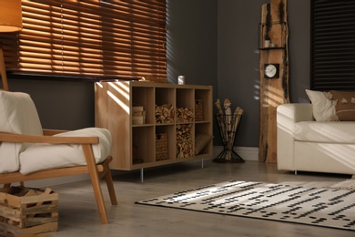 Photo of Shelving unit with stacked firewood and comfortable sofa in stylish room interior