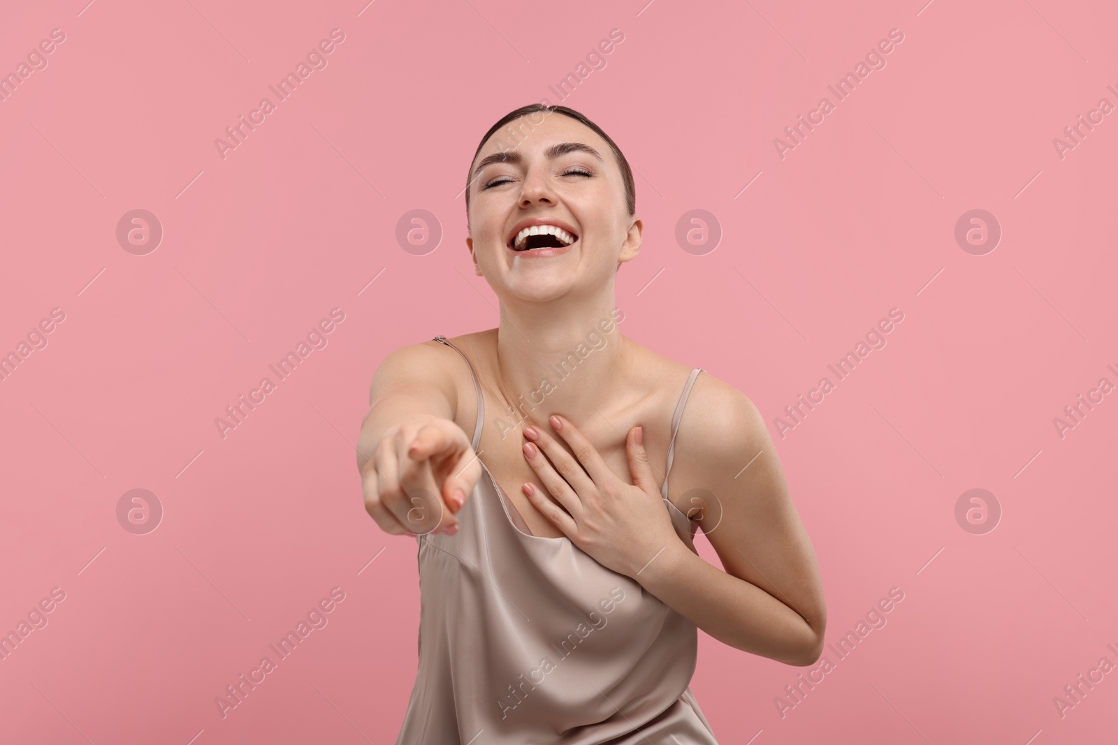 Photo of Beautiful woman pointing at something and laughing on pink background