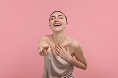 Photo of Beautiful woman pointing at something and laughing on pink background