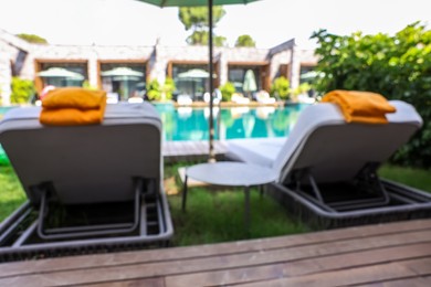 Photo of Sunbeds near swimming pool at luxury resort, blurred view