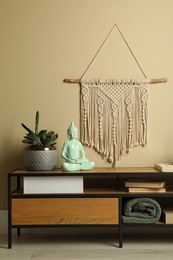 Photo of Beautiful macrame hanging on beige wall in room. Decorative element