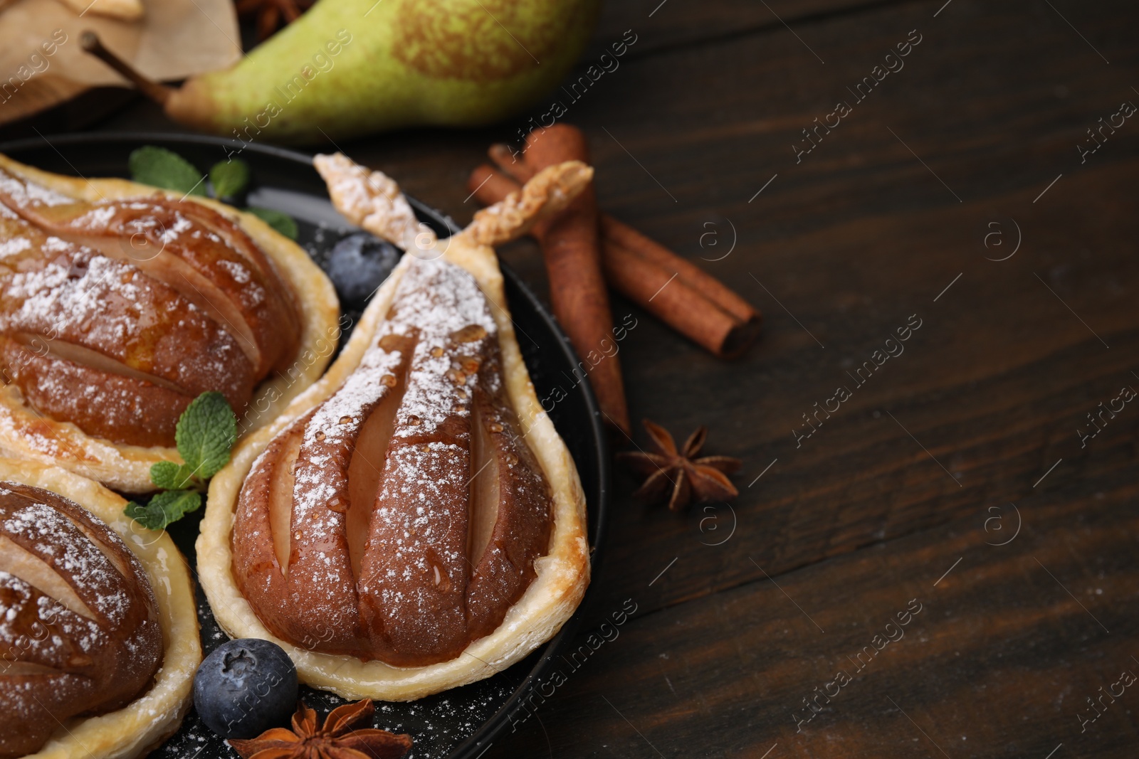 Photo of Delicious pears baked in puff pastry with powdered sugar served on wooden table, closeup. Space for text