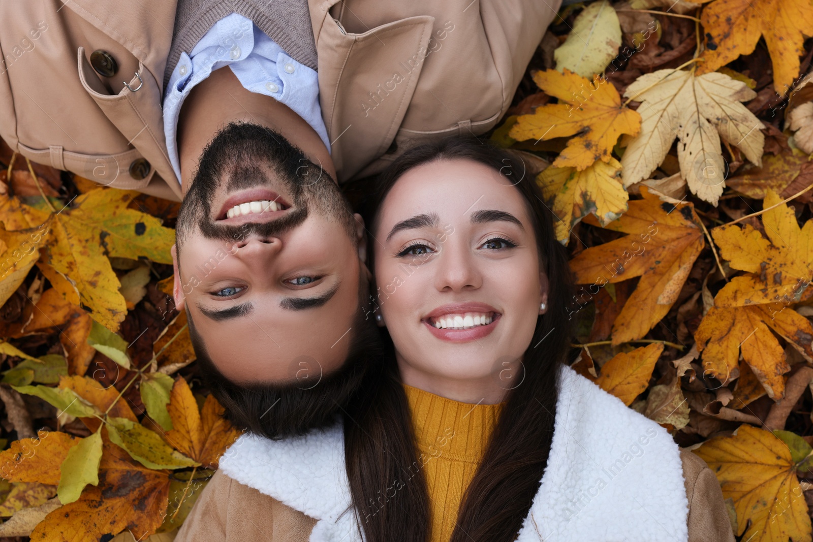 Photo of Happy young couple lying on dry leaves outdoors, top view