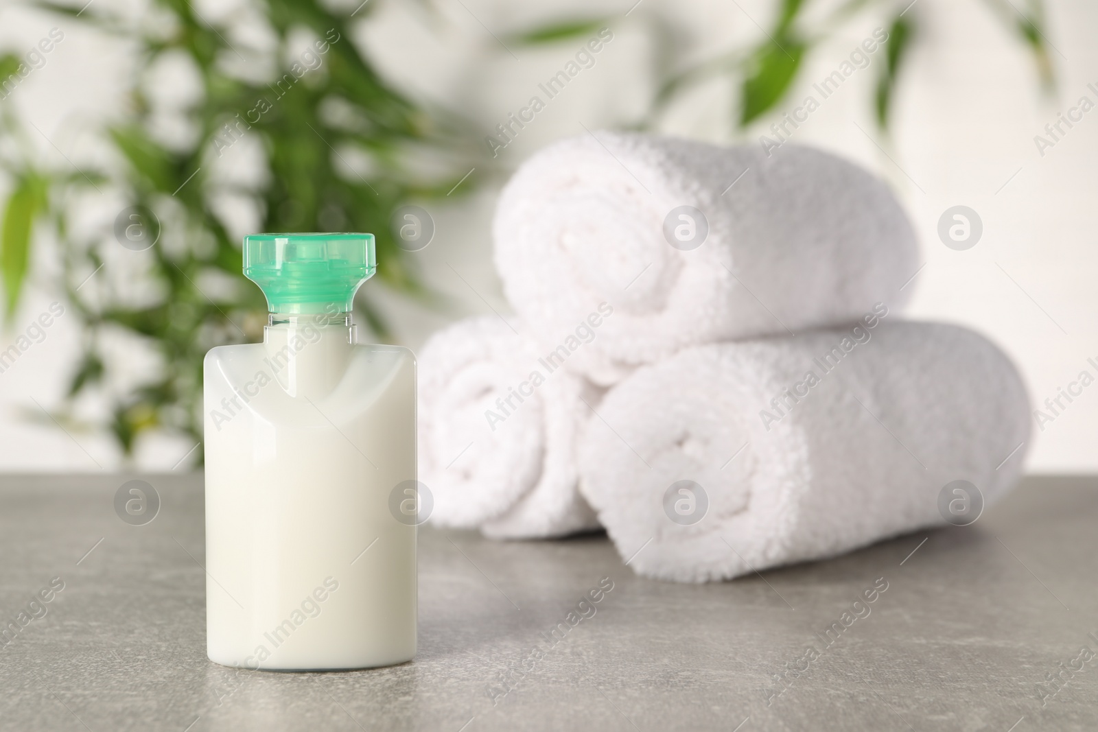 Photo of Mini bottle of cosmetic product and rolled towels on light grey table against blurred background