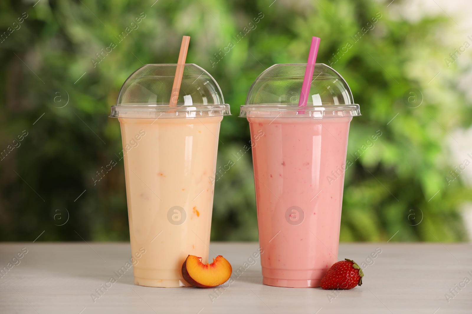 Photo of Plastic cups with different tasty smoothies and fresh fruits on wooden table outdoors