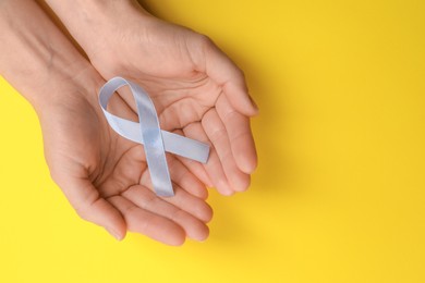 Photo of International Psoriasis Day. Woman with light blue ribbon as symbol of support on yellow background, top view. Space for text
