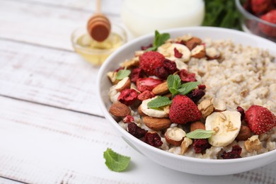 Photo of Delicious oatmeal with freeze dried berries, banana, nuts and mint on white wooden table, closeup. Space for text