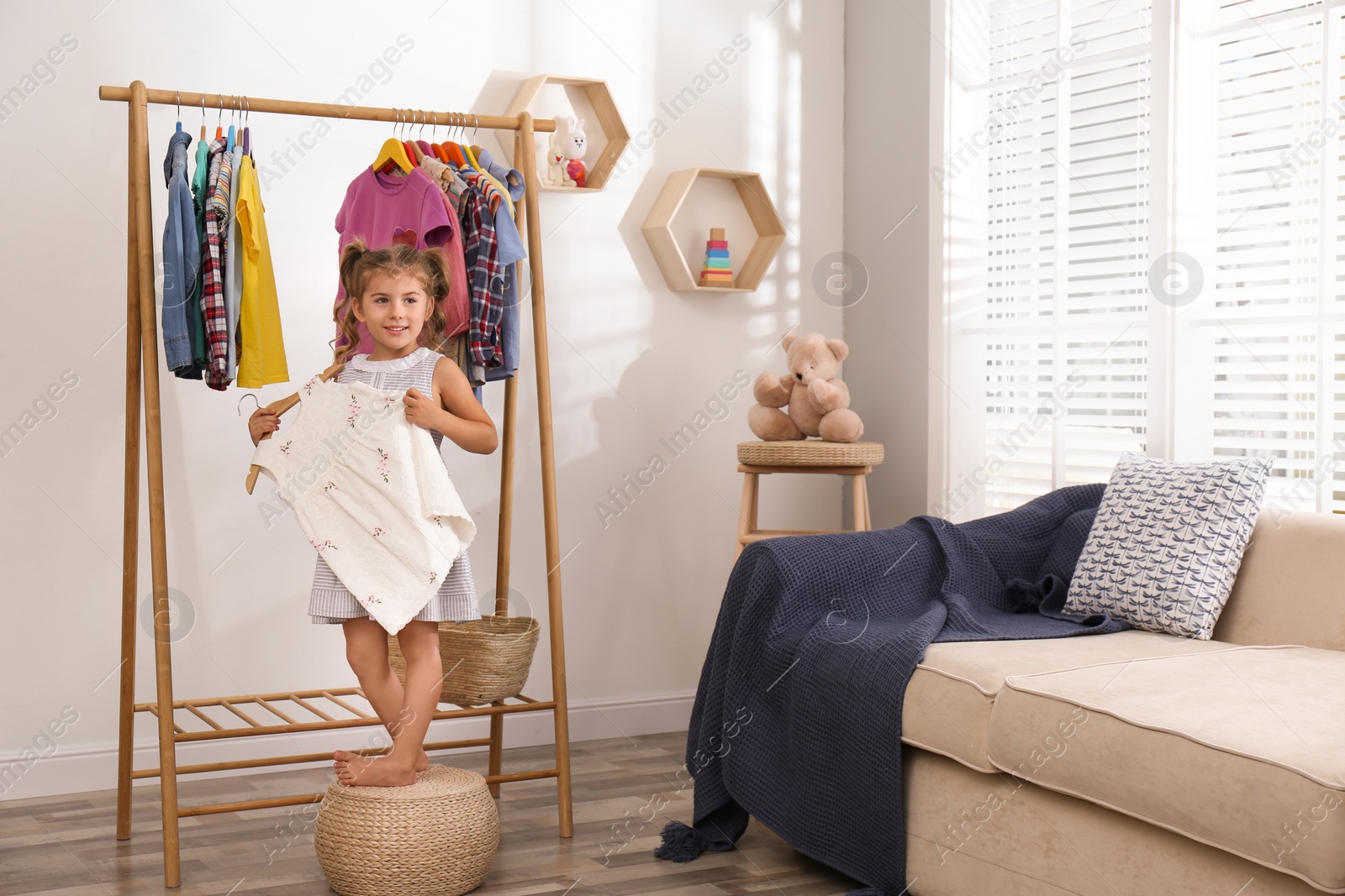 Photo of Little girl choosing clothes on rack in living room