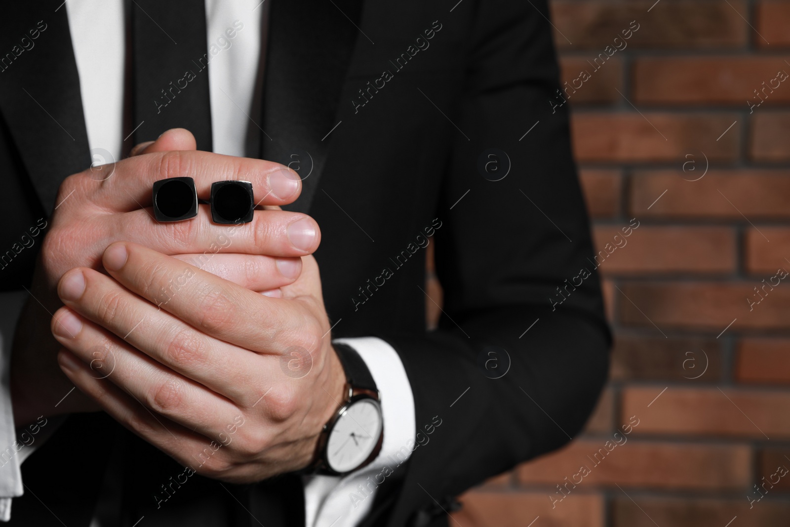 Photo of Man holding stylish cufflinks near brick wall, closeup. Space for text