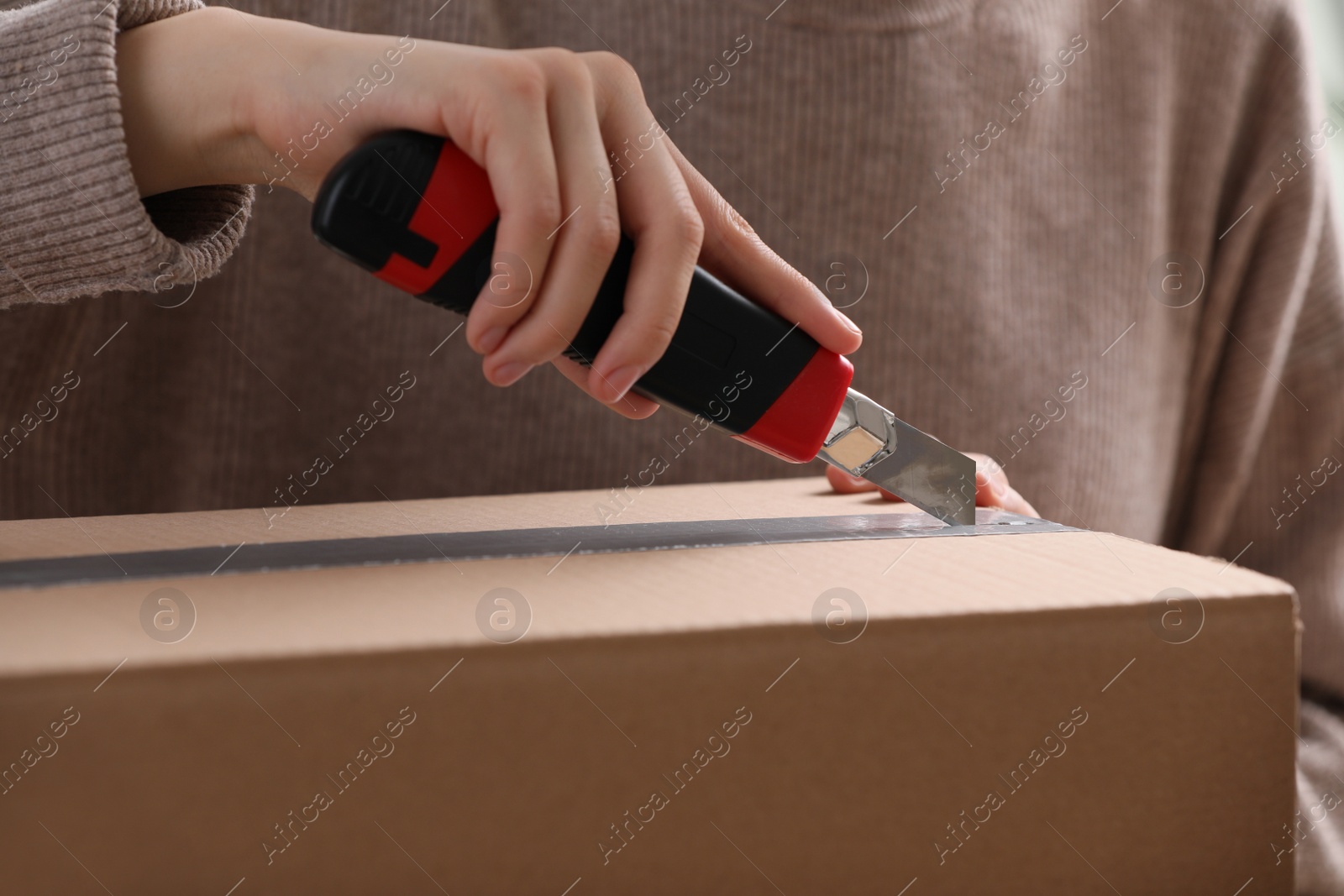 Photo of Young woman using utility knife to open parcel, closeup