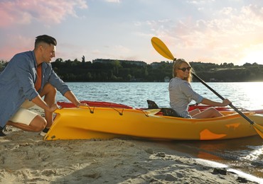 Photo of Man helping woman on kayak at riverside. Summer activity