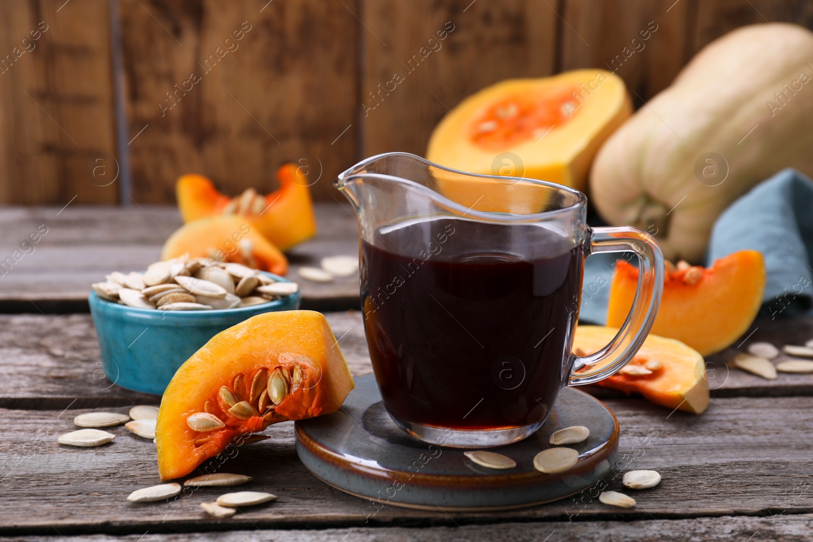 Photo of Fresh pumpkin seed oil in glass pitcher on wooden table