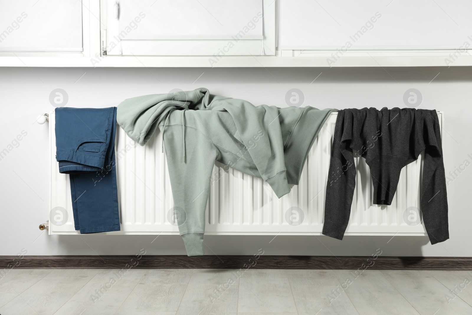 Photo of Pants, hoodie and turtleneck sweater on heating radiator near window indoors