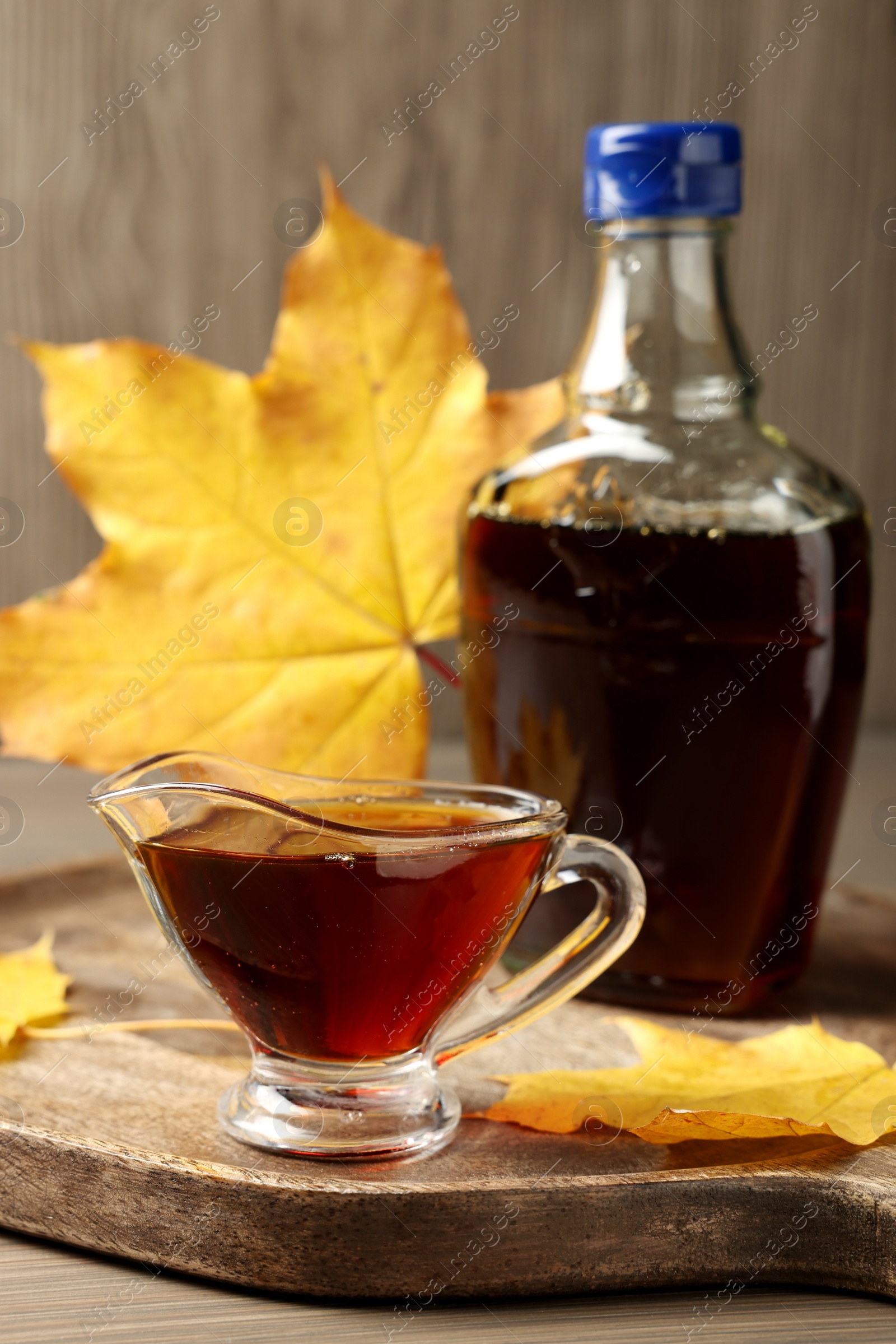 Photo of Bottle and gravy boat with tasty maple syrup on wooden table