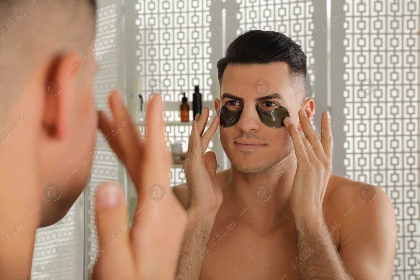 Photo of Man applying dark under eye patches near mirror at home