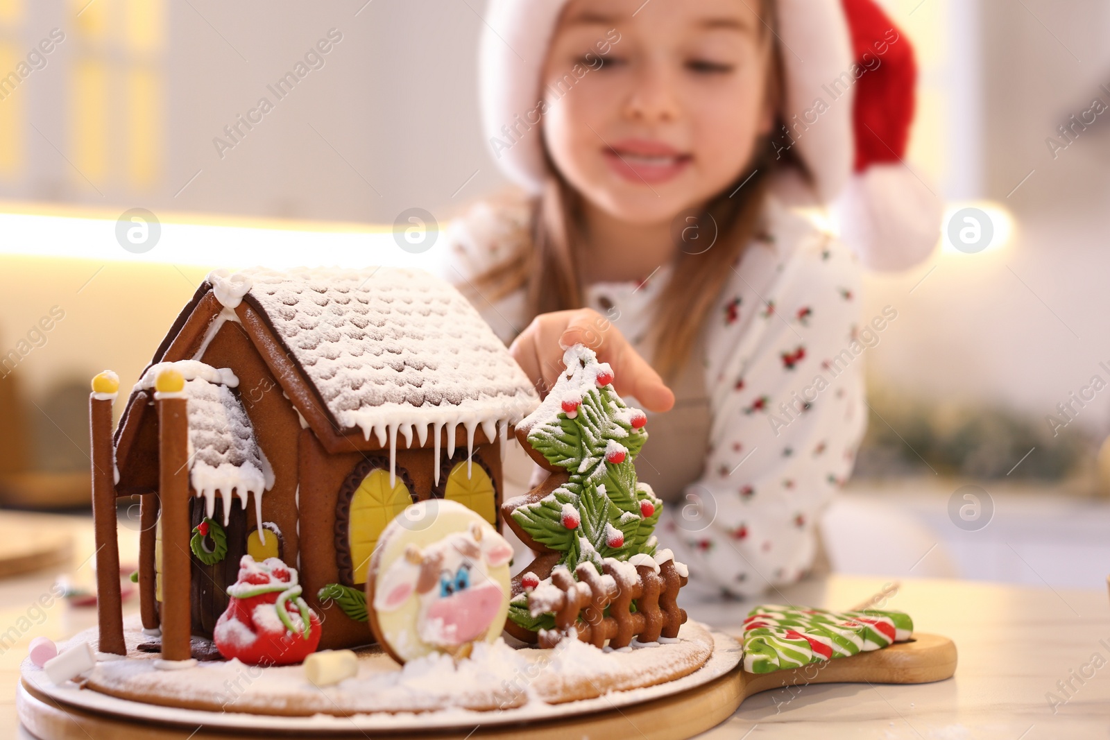 Photo of Cute little girl near gingerbread house indoors