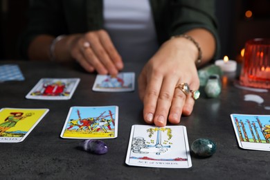 Photo of Fortune teller predicting future on spread of tarot cards at grey table indoors, closeup