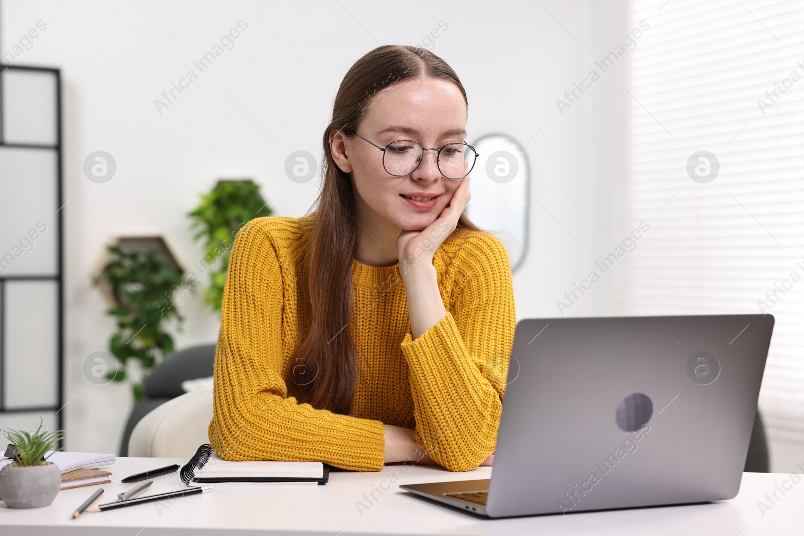 Photo of E-learning. Young woman using laptop during online lesson at white table indoors