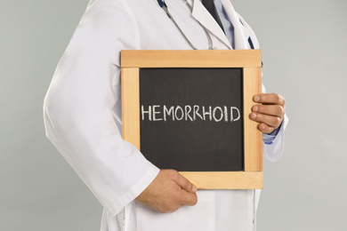 Photo of Doctor holding blackboard with word HEMORRHOID on light grey background, closeup