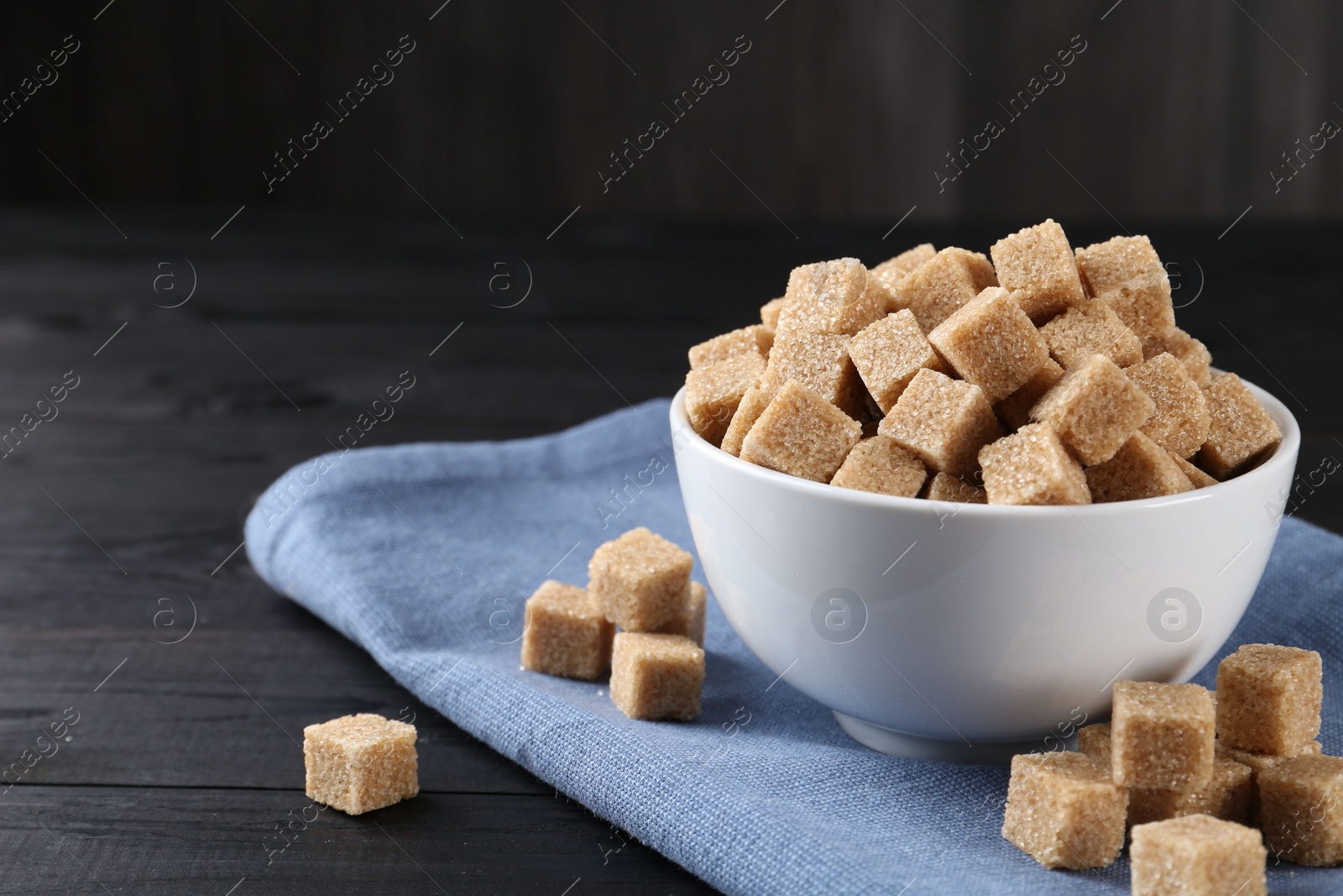 Photo of Brown sugar cubes on black wooden table, space for text