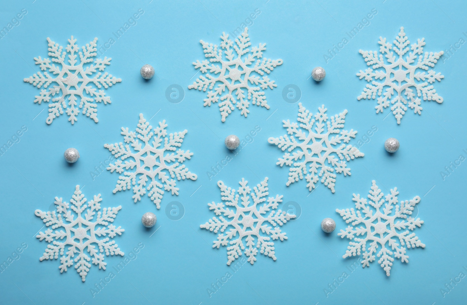 Photo of Beautiful snowflakes and decorative balls on light blue background, flat lay