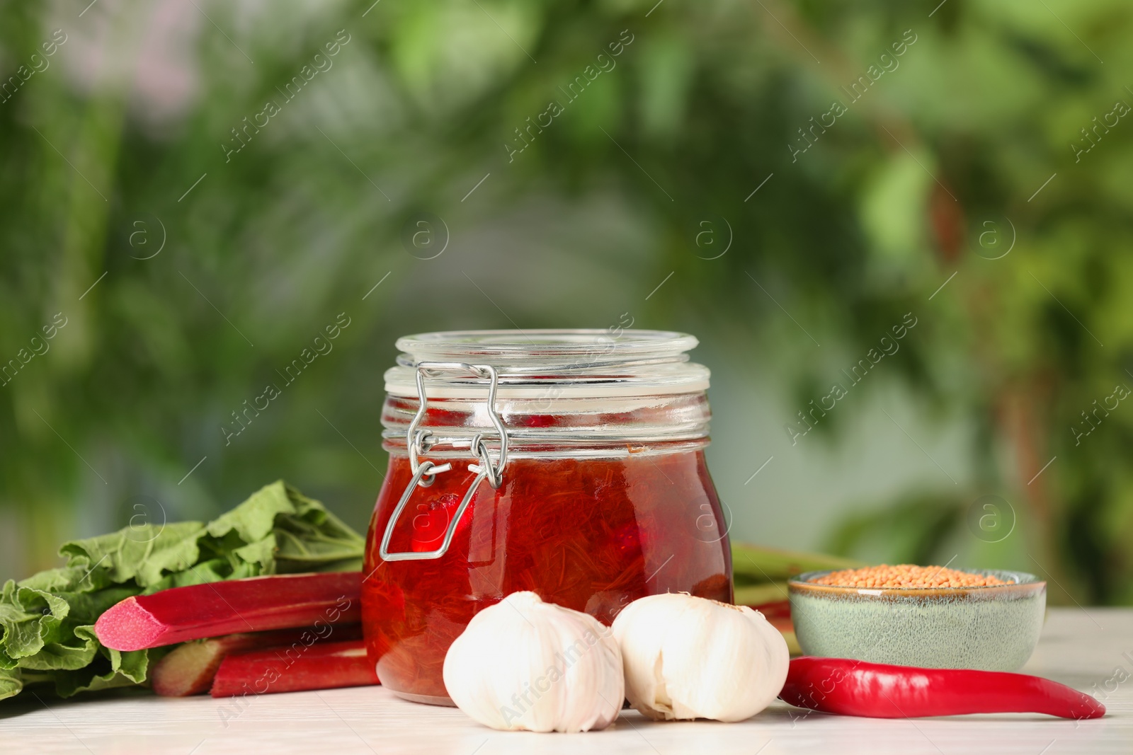 Photo of Tasty rhubarb sauce and ingredients on white table against blurred background , space for text