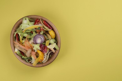 Peels of fresh vegetables in bowl on yellow background, top view. Space for text