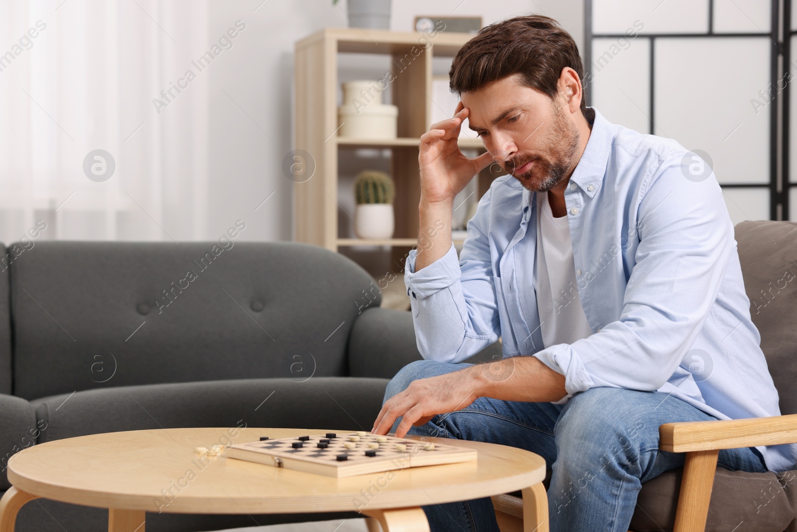 Photo of Thoughtful man playing checkers at home. Space for text