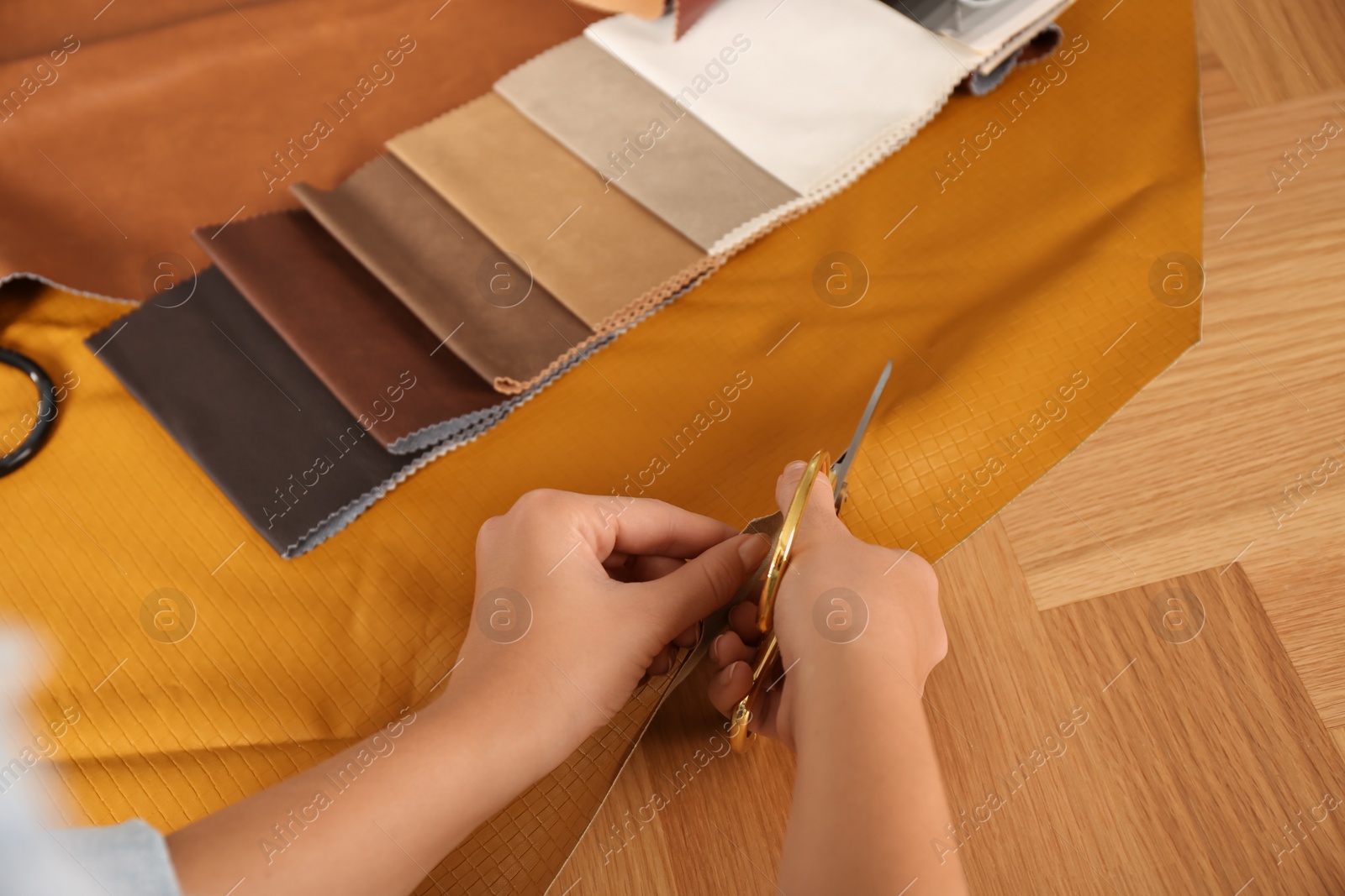 Photo of Woman cutting orange leather with scissors at wooden table, closeup