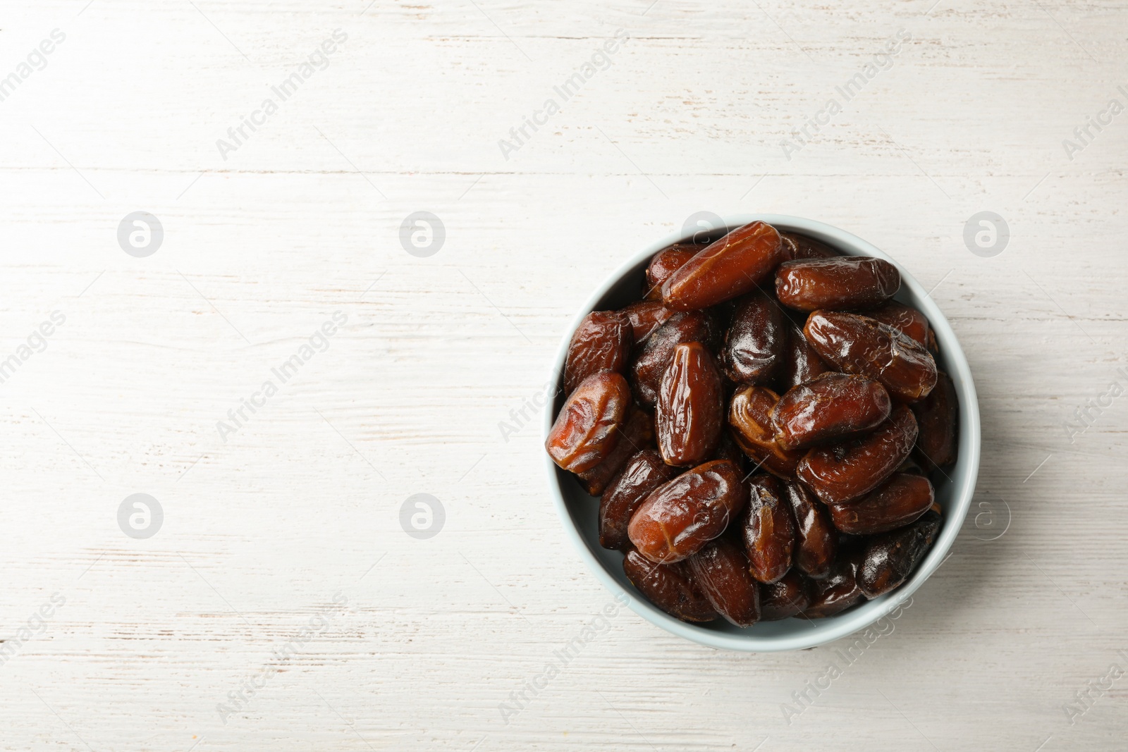 Photo of Bowl of sweet dates on wooden background, top view with space for text. Dried fruit as healthy snack