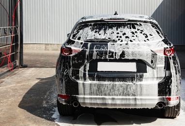 Photo of Luxury automobile covered with foam at car wash, back view
