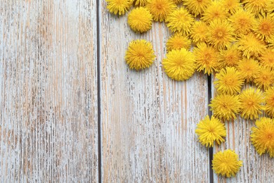 Photo of Beautiful yellow dandelions on light wooden table, flat lay. Space for text