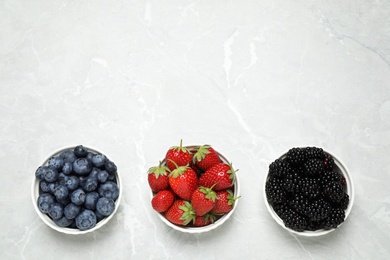 Photo of Different ripe berries on light marble table, flat lay. Space for text