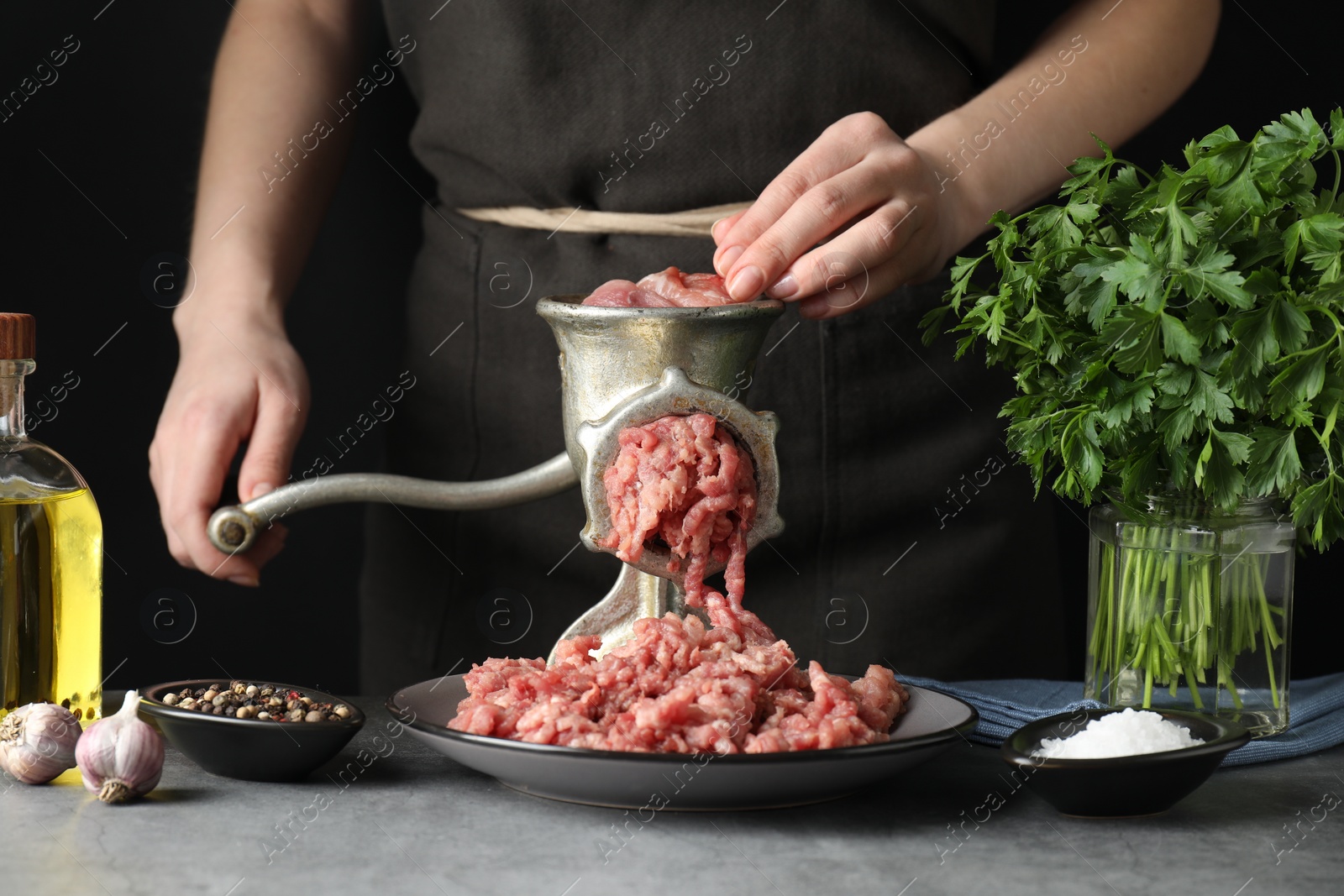 Photo of Woman making beef mince with manual meat grinder at grey table, closeup