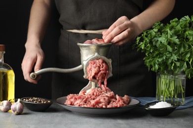 Photo of Woman making beef mince with manual meat grinder at grey table, closeup