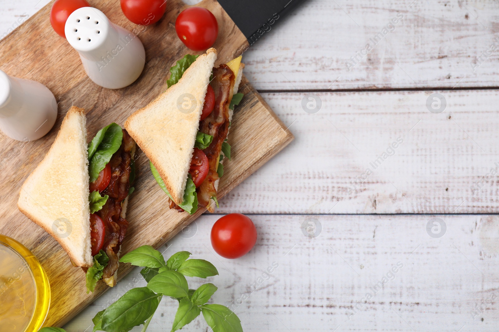 Photo of Delicious sandwiches with fried bacon, spices and products on wooden rustic table, flat lay. Space for text