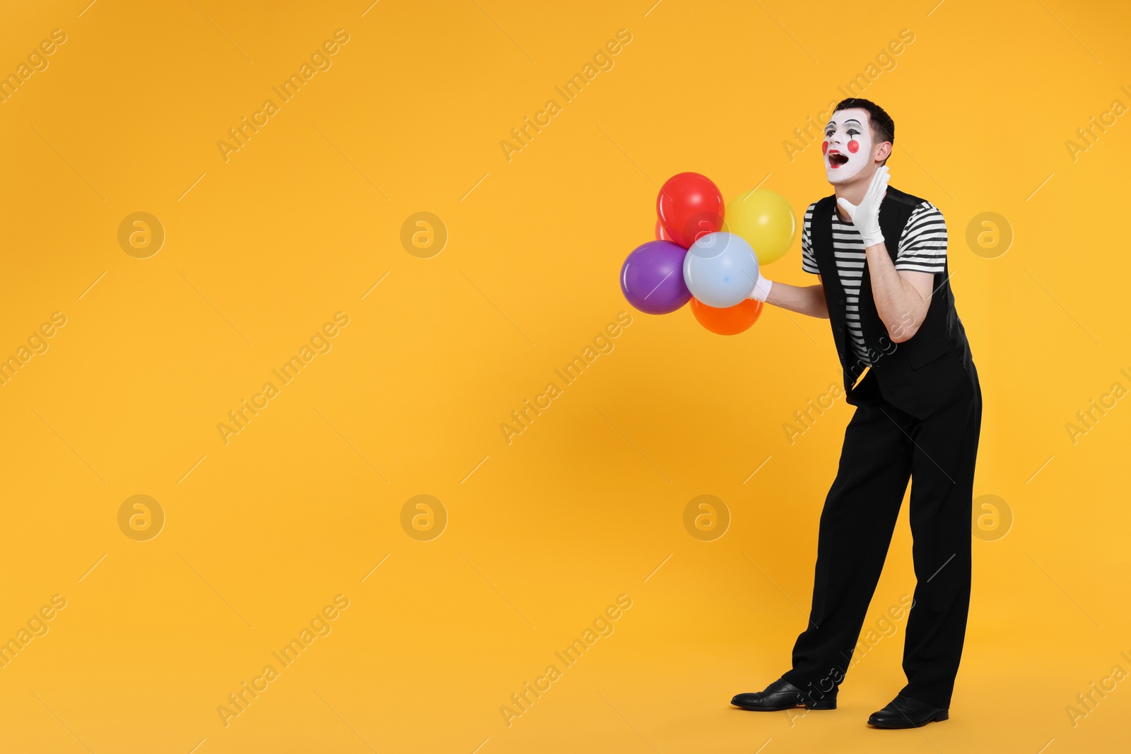 Photo of Funny mime artist with balloons screaming on orange background. Space for text