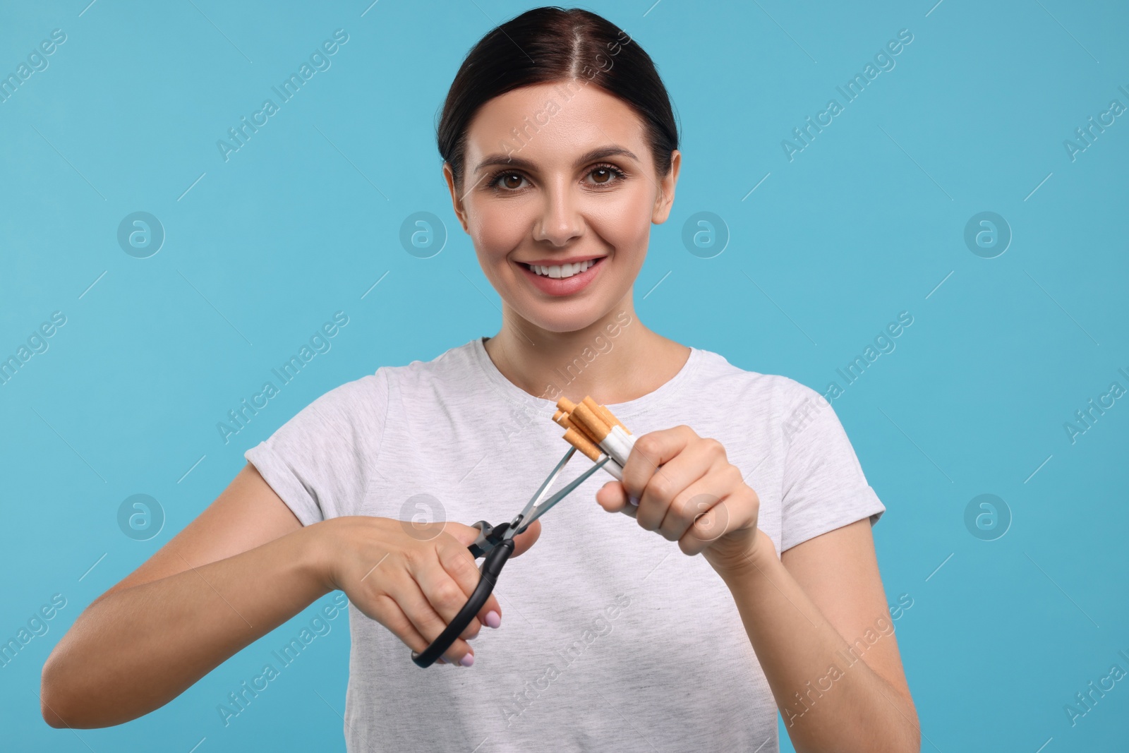 Photo of Stop smoking concept. Happy young woman cutting cigarettes on light blue background