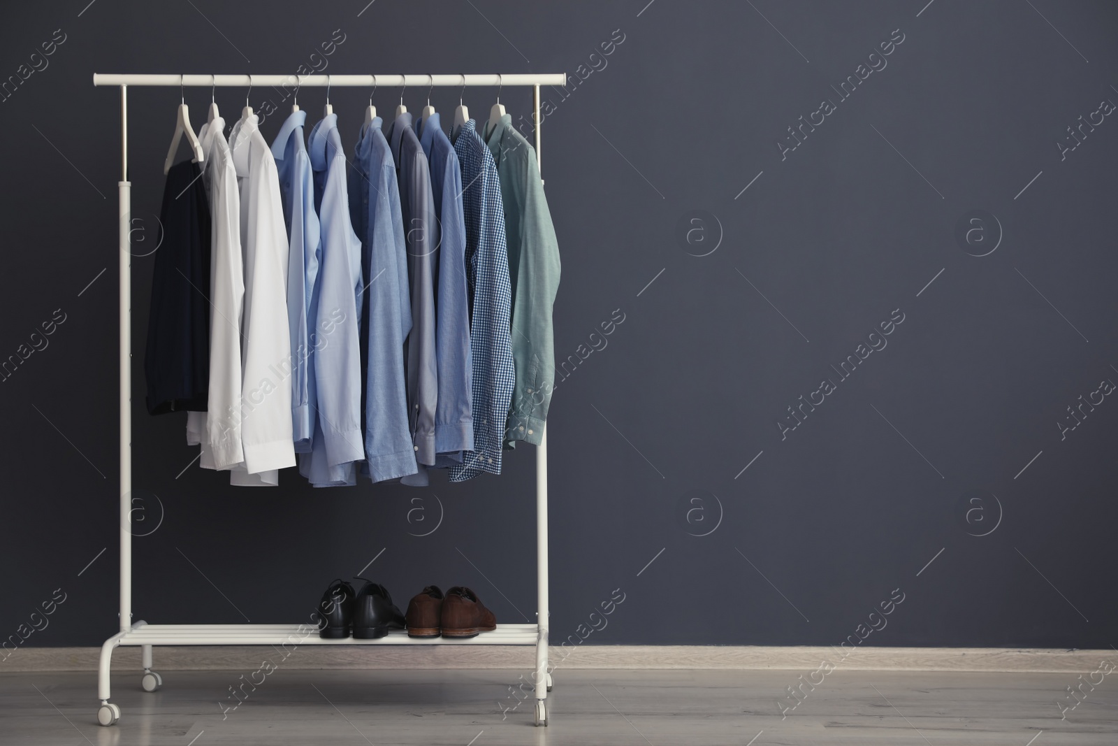 Photo of Wardrobe rack with men's clothes near grey wall. Space for text