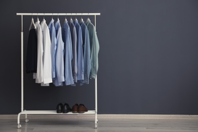 Wardrobe rack with men's clothes near grey wall. Space for text