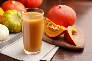 Photo of Tasty pumpkin juice in glass and different pumpkins on wooden table