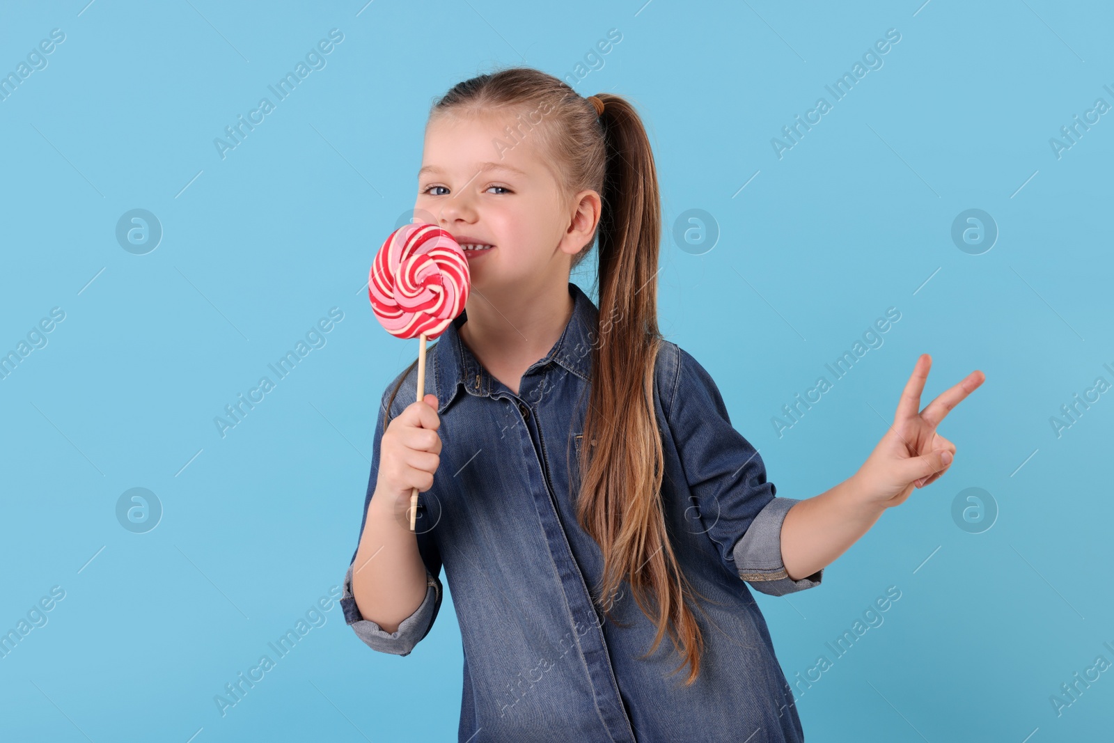 Photo of Happy little girl with bright lollipop swirl on light blue background