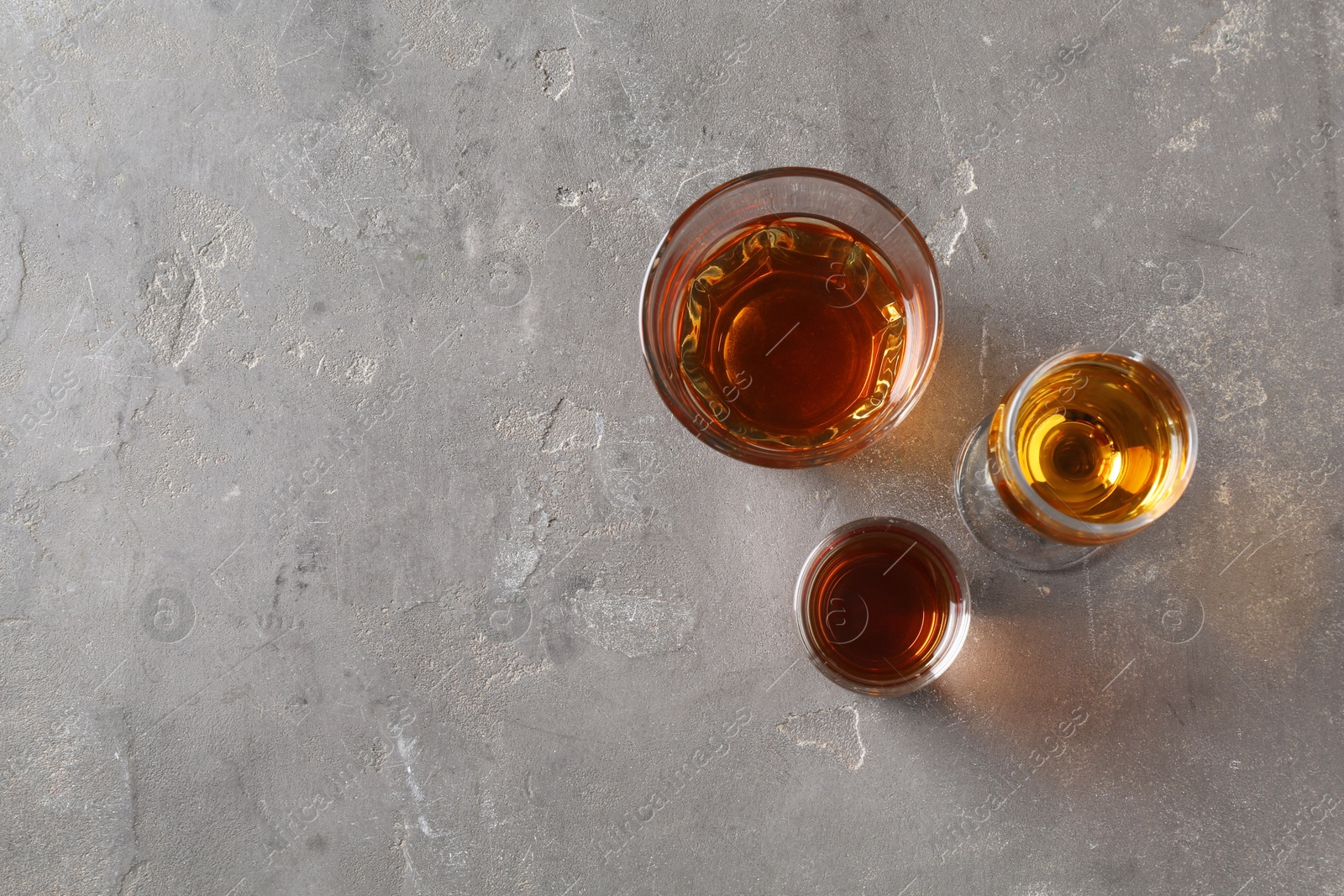 Photo of Different delicious liqueurs in glasses on grey table, flat lay. Space for text