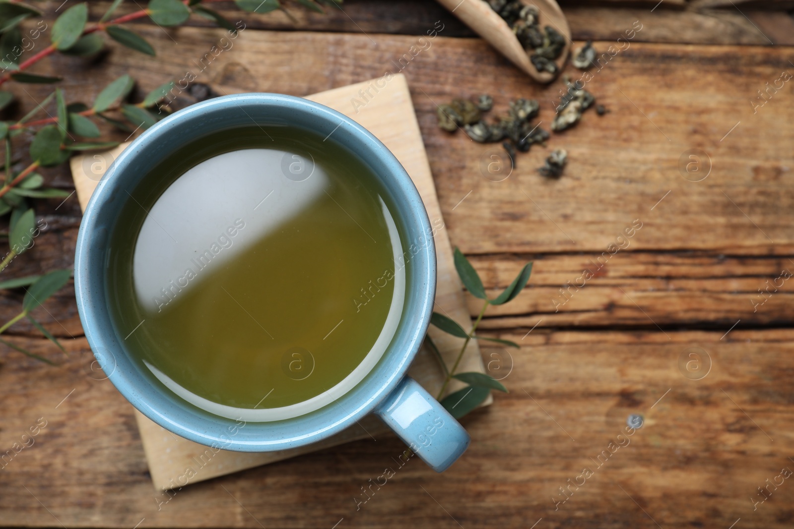 Photo of Cup of green tea and eucalyptus leaves on wooden table, flat lay. Space for text