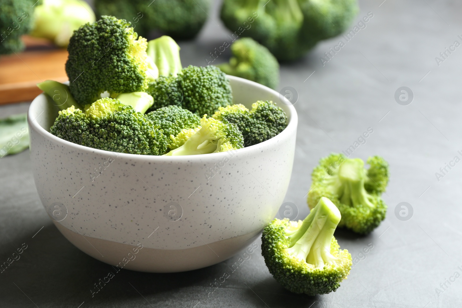 Photo of Bowl and fresh broccoli on grey table, closeup