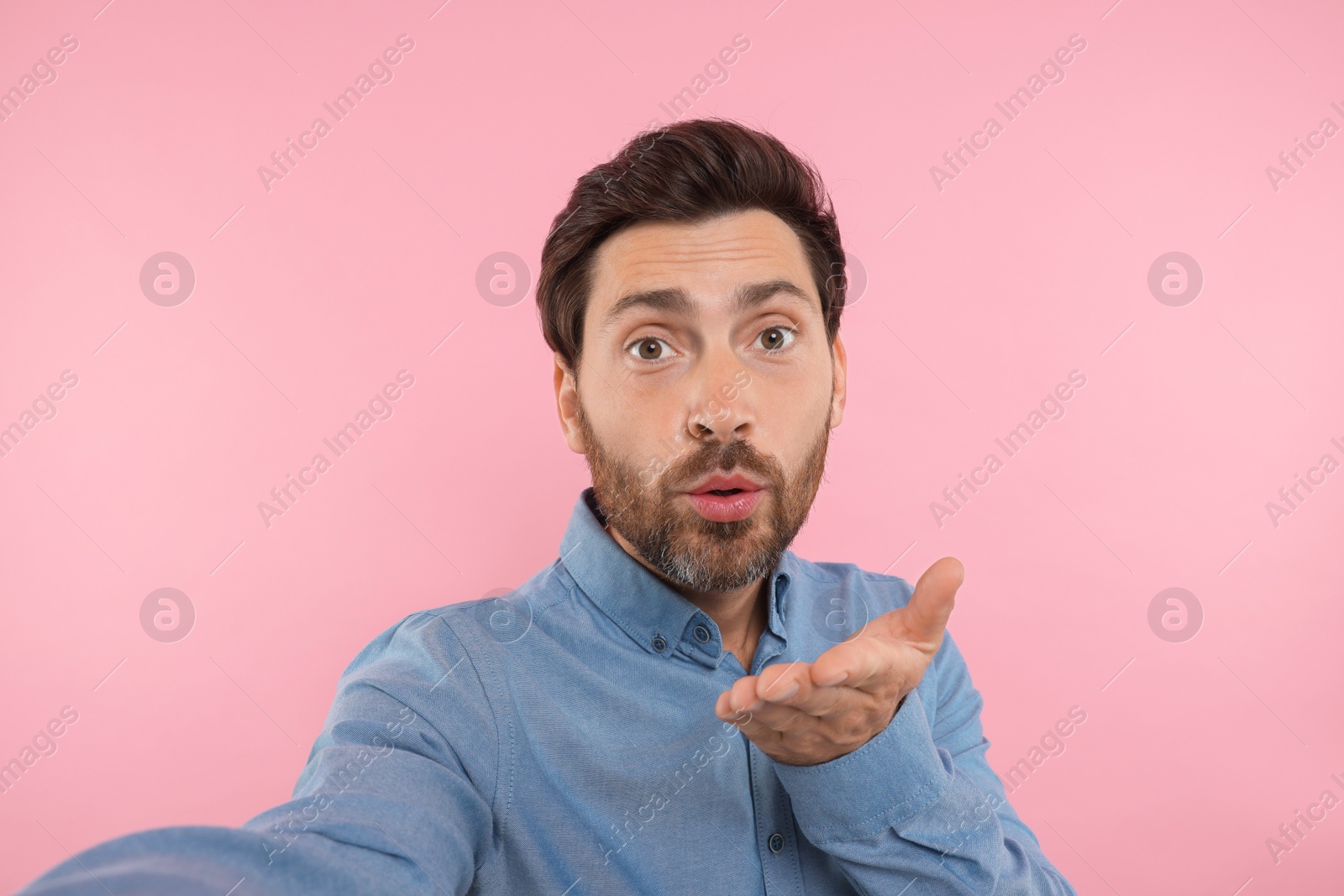 Photo of Man taking selfie and blowing kiss on pink background