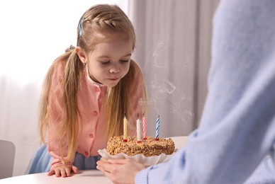 Photo of Birthday celebration. Mother holding tasty cake with candles near her daughter indoors