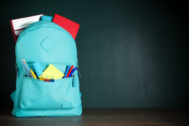 Photo of Stylish backpack with different school stationery on table against chalkboard. Space for text